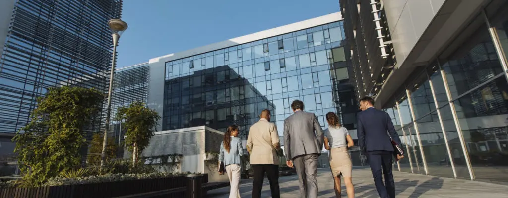 Plano trasero de cinco empresarios caminando junto a un edificio de oficinas