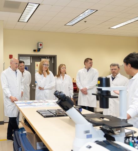 Personas con batas blancas de laboratorio de pie junto a los microscopios en un laboratorio.