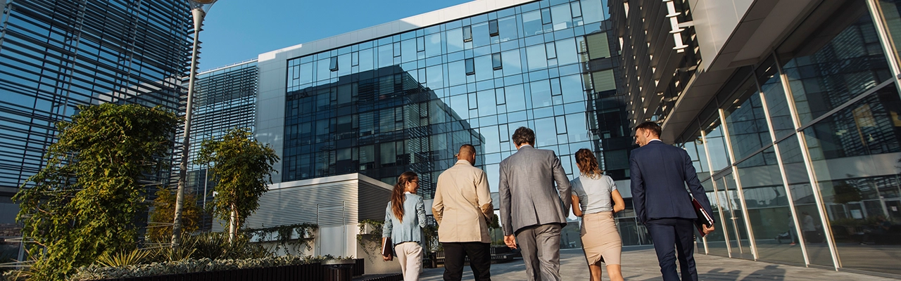 Plano trasero de cinco empresarios caminando junto a un edificio de oficinas