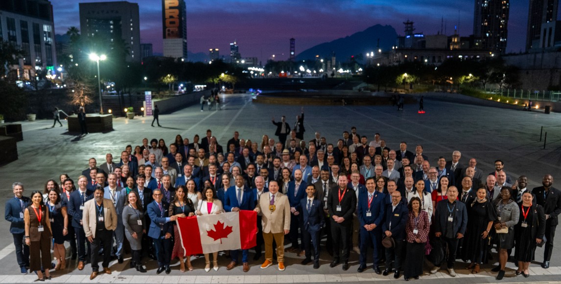 Grupo de personas al anochecer con la bandera canadiense, el paisaje urbano y las montañas de fondo, destacando la vibrante economía y los activos naturales de Columbia Británica.